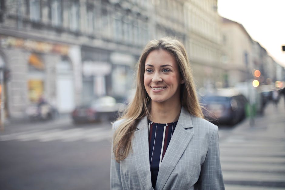Smiling woman in a gray blazer standing on a city street with blurred buildings and cars in the background.